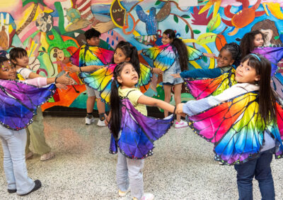 Young children in a hallway pose with colorful wings on.