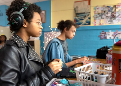 Students in a classroom making beaded bracelets.
