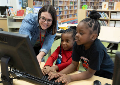 A teacher helps two young students use a computer.