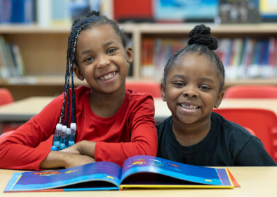 Two young students in a library, smiling at the camera.