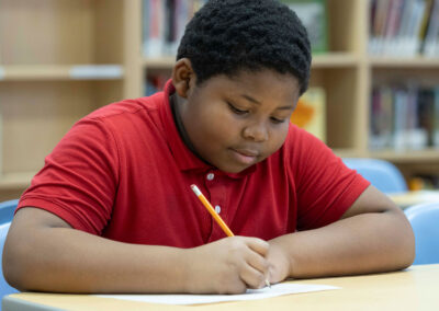 A boy in a library, writing.