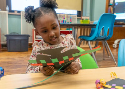 A young girl at a table weaving with paper.