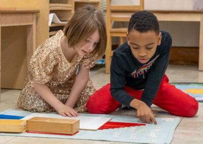 Two students on the floor using Montessori tools.