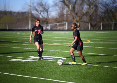 Two girls on a turf field playing soccer.