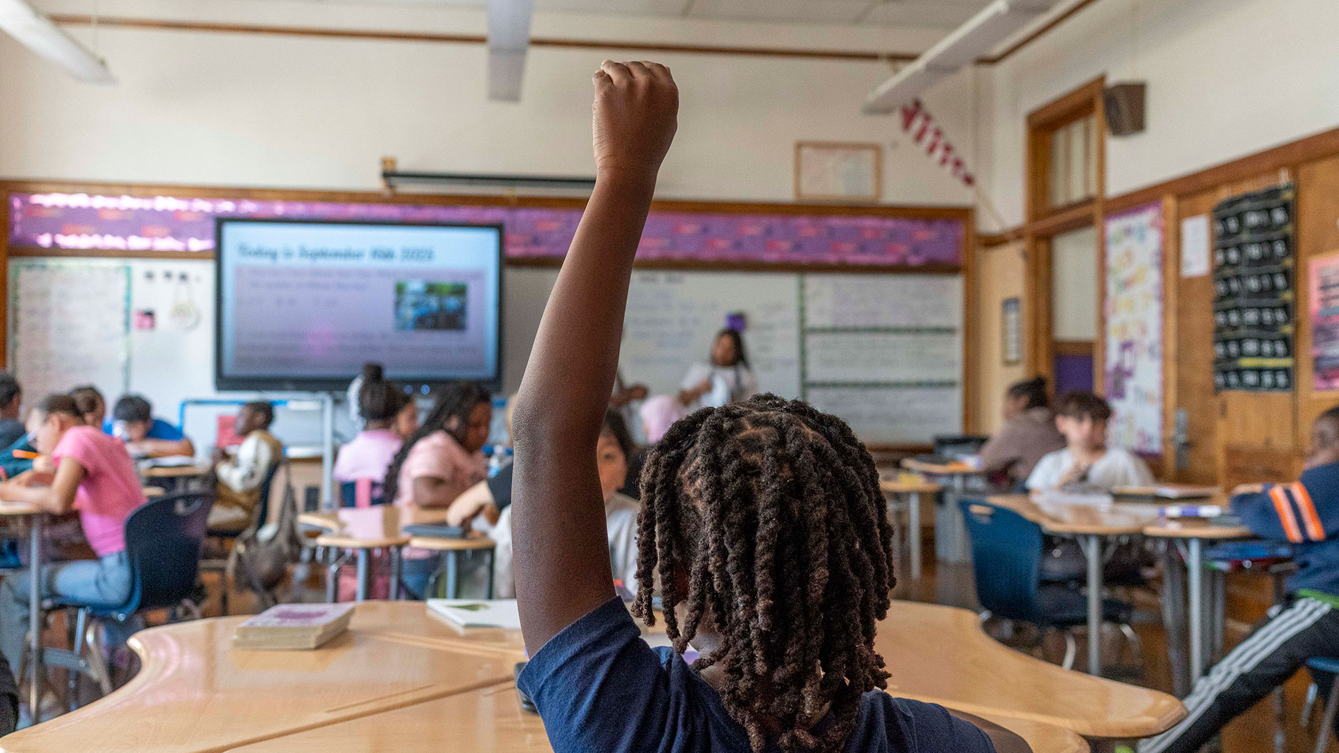 A student in a classroom raises his hand.