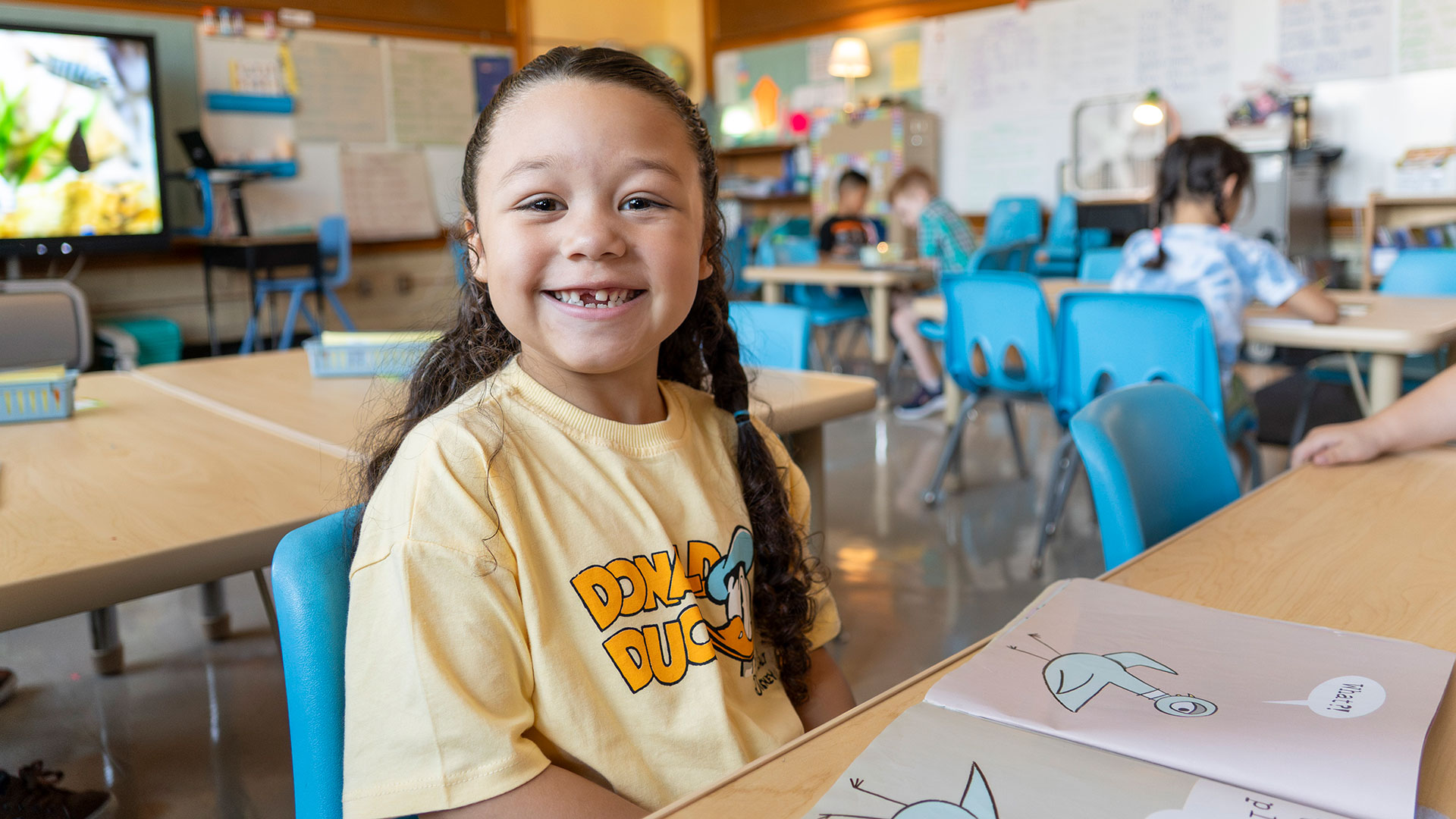 A young child smiles while reading a book.