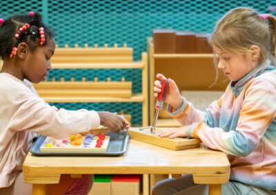 Two young girls sit at a small table and practice their fine motor skills.