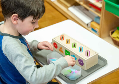 A young student putting colored shapes into a small box.
