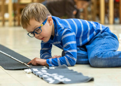 A young boy with glasses on the floor counting beads.
