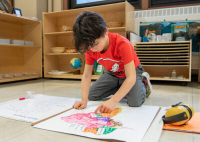 A young boy on the floor coloring a map of South America.