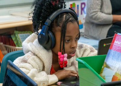 A young student with headphones looks at her computer screen.