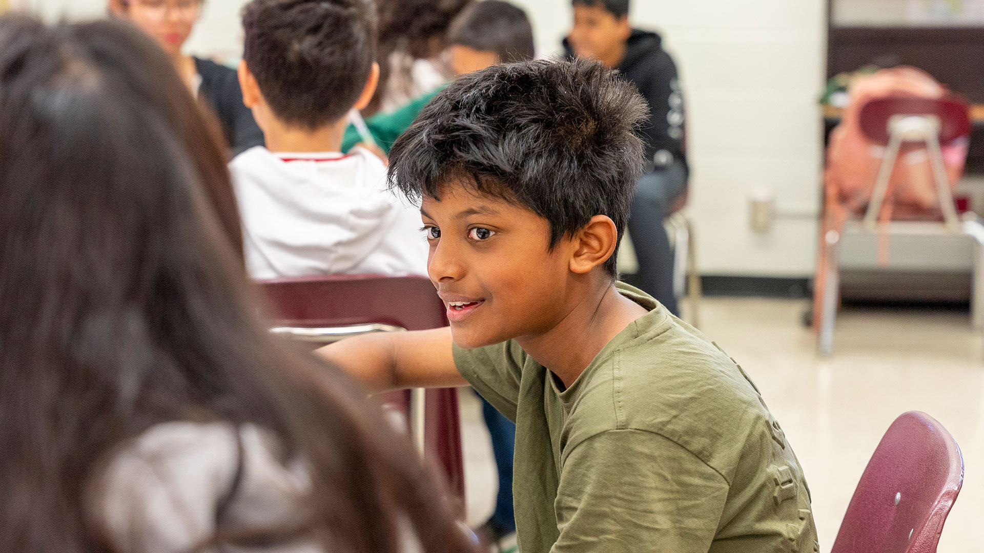 A child smiles while talking to another child in a classroom.