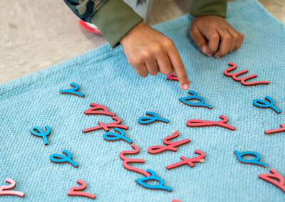 Close up view of a young hand pointing to cursive letters made of wood.