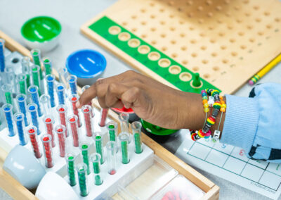 Small test tubes full of colorful beads in a tray as a young hand pulls one test tube from the tray.