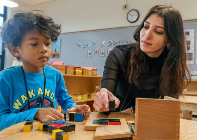 A teacher and her young student sit at a table and work with blocks.