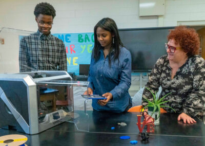 A teacher watches as students use a 3D printer.