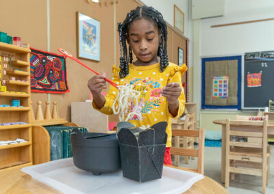 A young girl using chopsticks to pick up noodles that are made of yarn.