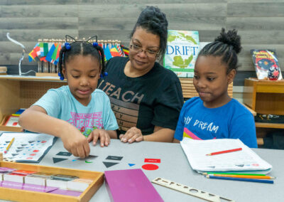 A teacher watches as two students learn shapes.