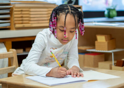 A young student at a desk writing in a notebook.