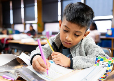 A young child in a classroom writing in a workbook.