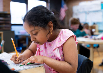 A student in a classroom practices writing in a workbook.