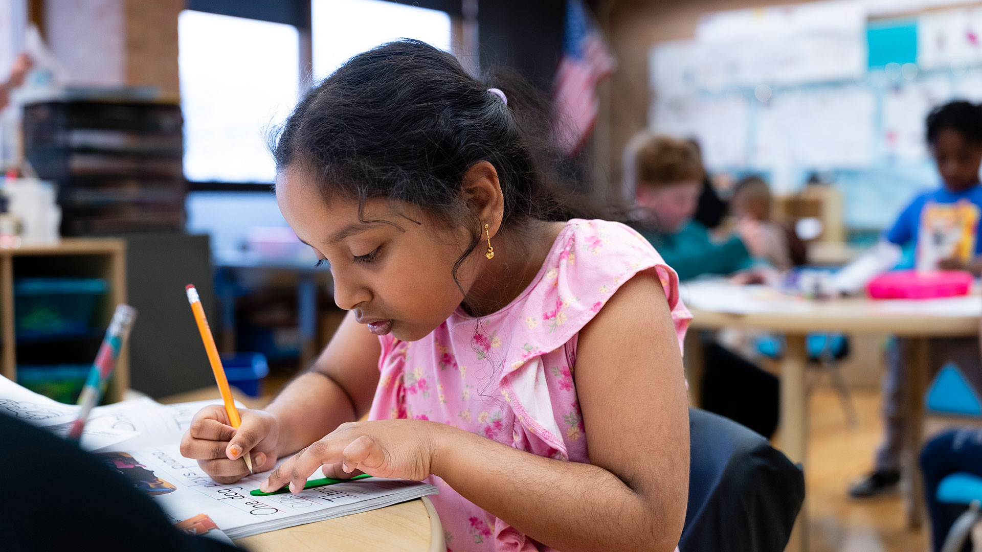 A student in a classroom practices writing in a workbook.