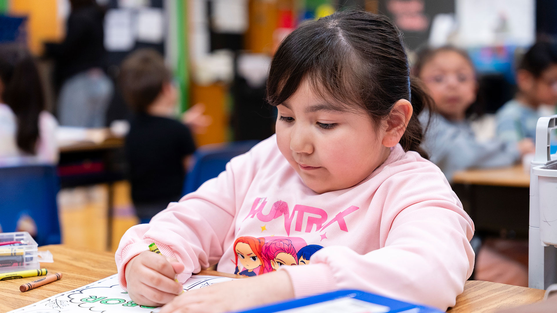 A young child in a classroom coloring.