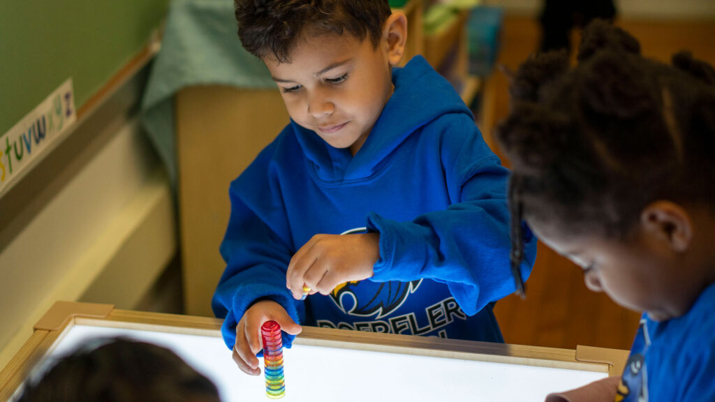 Young students stack blocks on a light table.