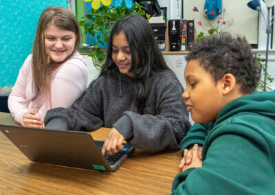 Three students look at a laptop.