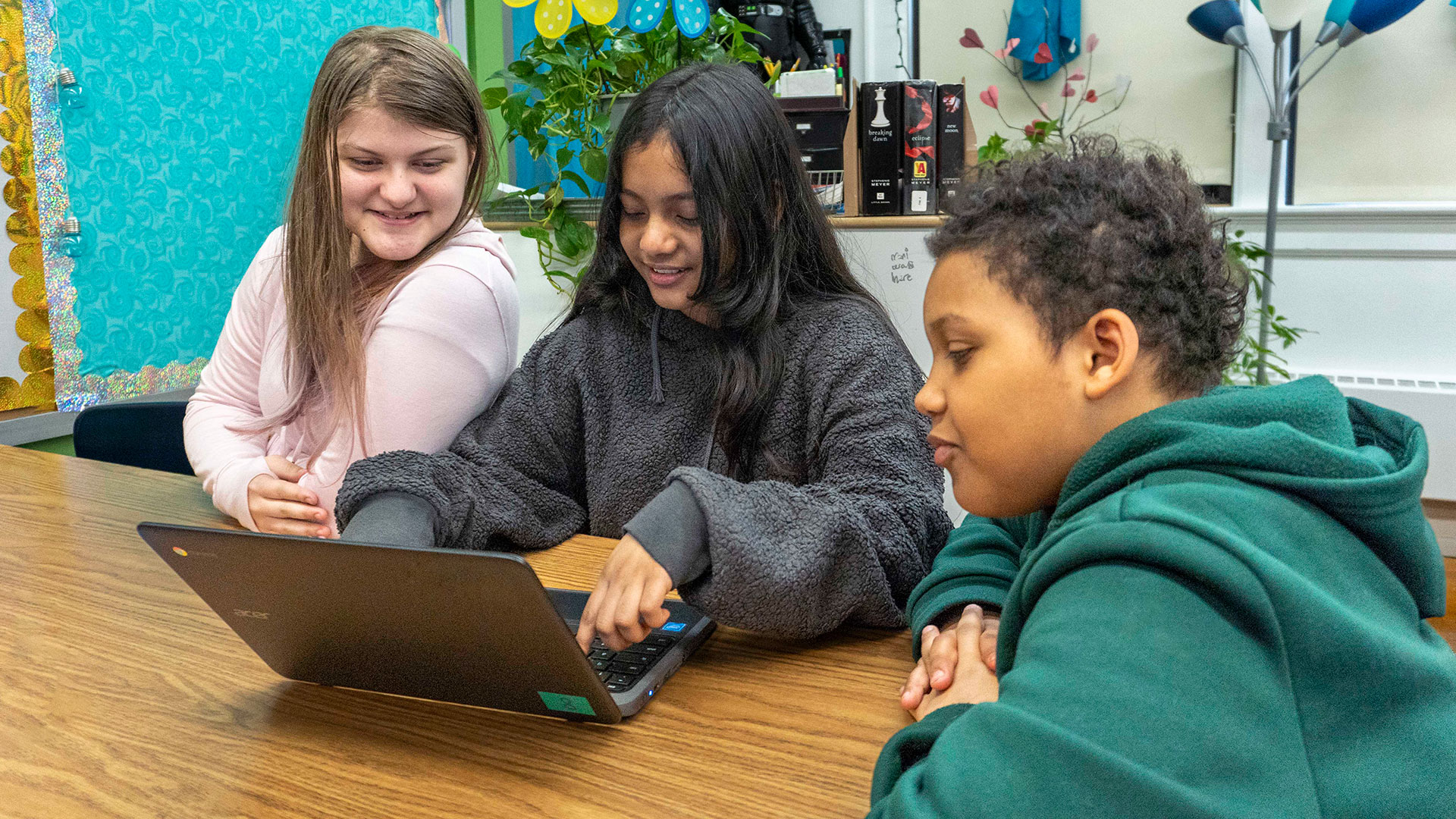 Three students look at a laptop.