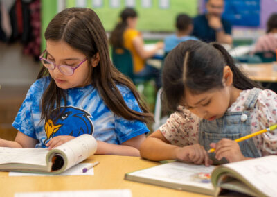 Two young girls sit at a table in a classroom and work on an assignment.