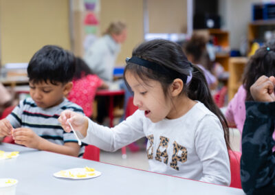 Young children in a classroom work on at art project.