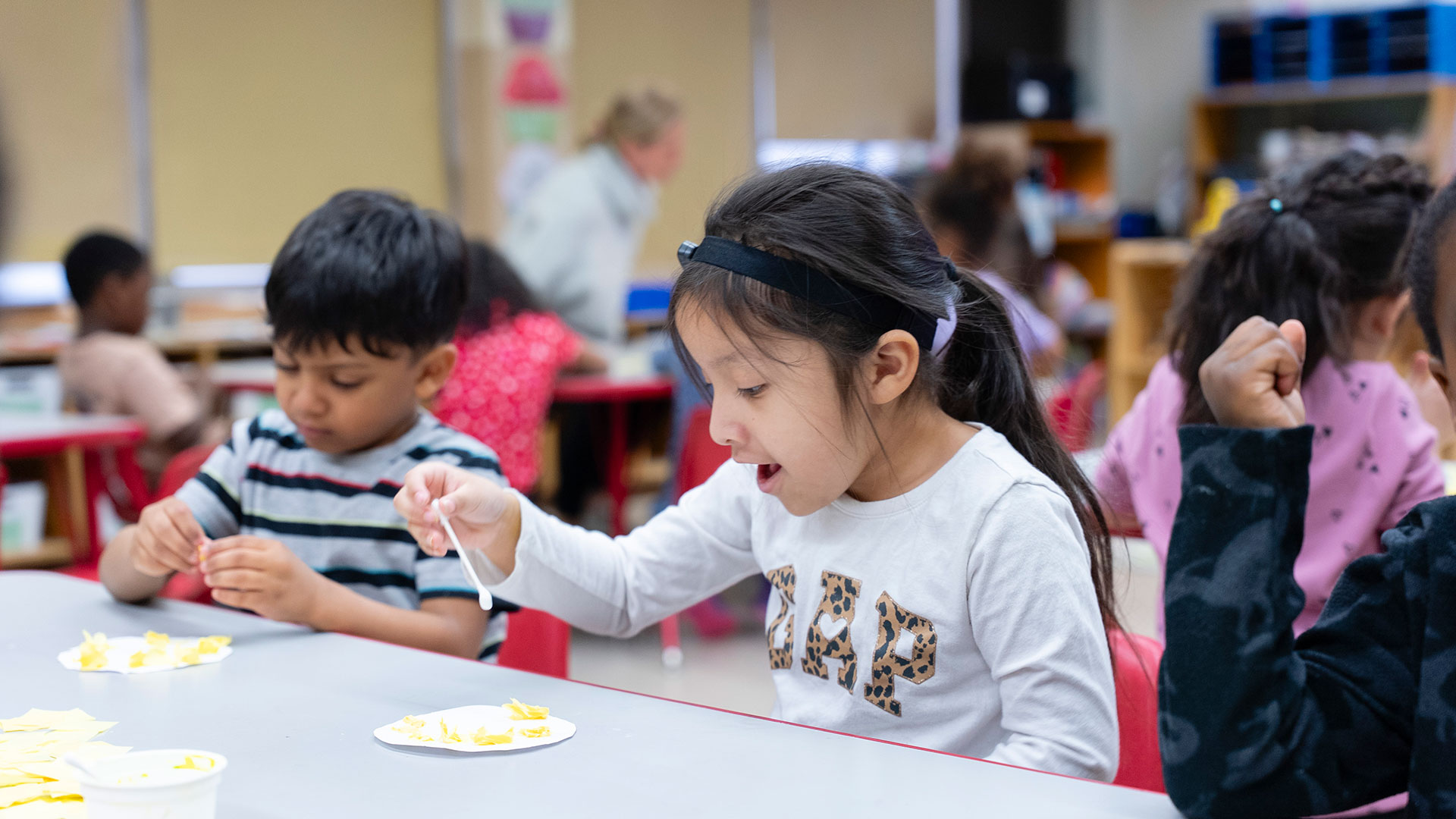 Young children in a classroom work on at art project.