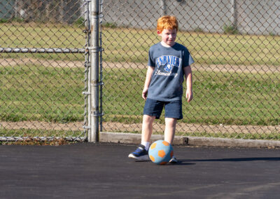 A young child on blacktop with a soccer ball.