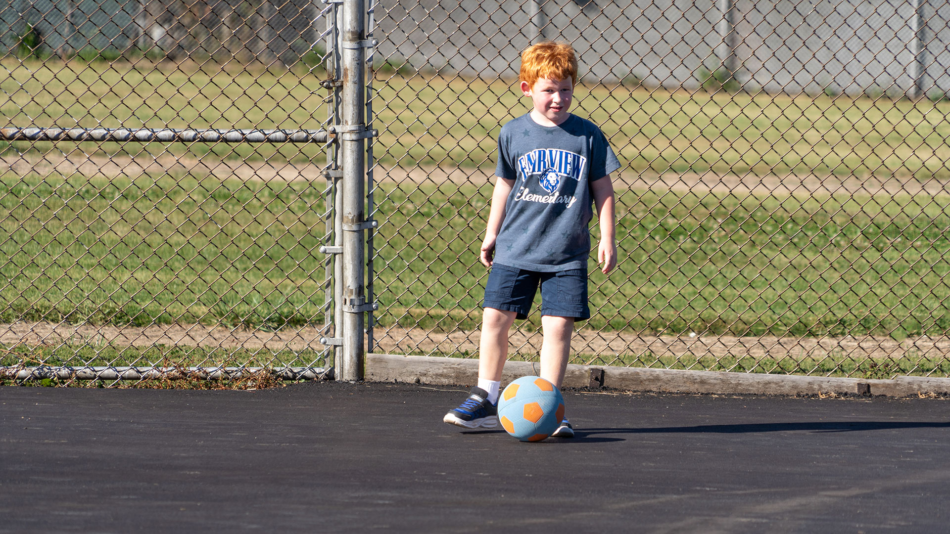 A young child on blacktop with a soccer ball.