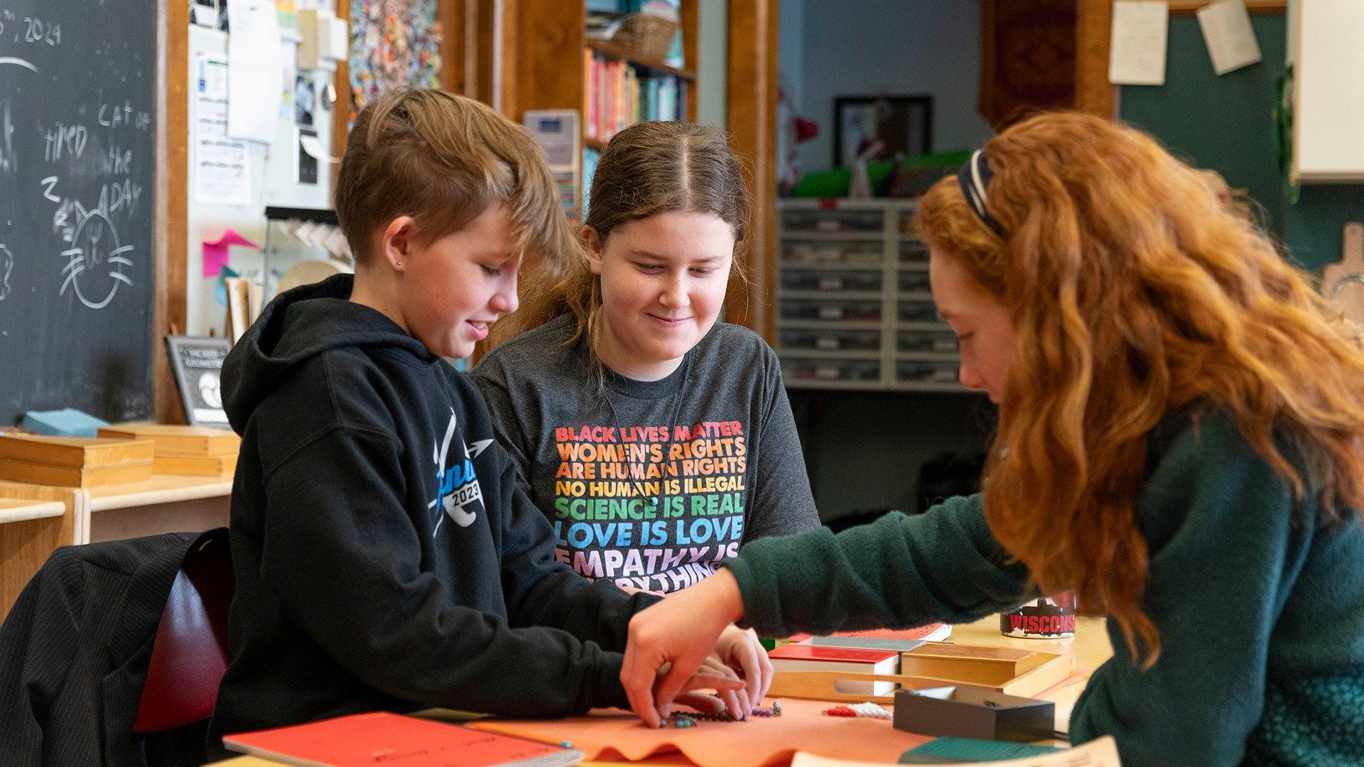 Students smile as they sit at a table and sort beads.