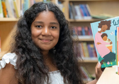 A girl in a library pulling a book from the shelf.