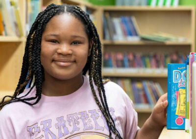 A girl in a library pulling a book from the shelf.