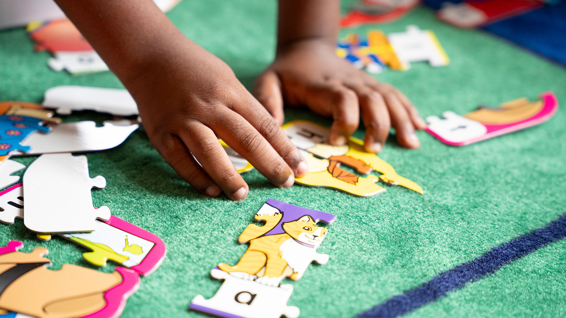Close-up of a child's hand putting puzzle pieces together.