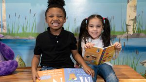 Two young students sit on a bench and look at books.