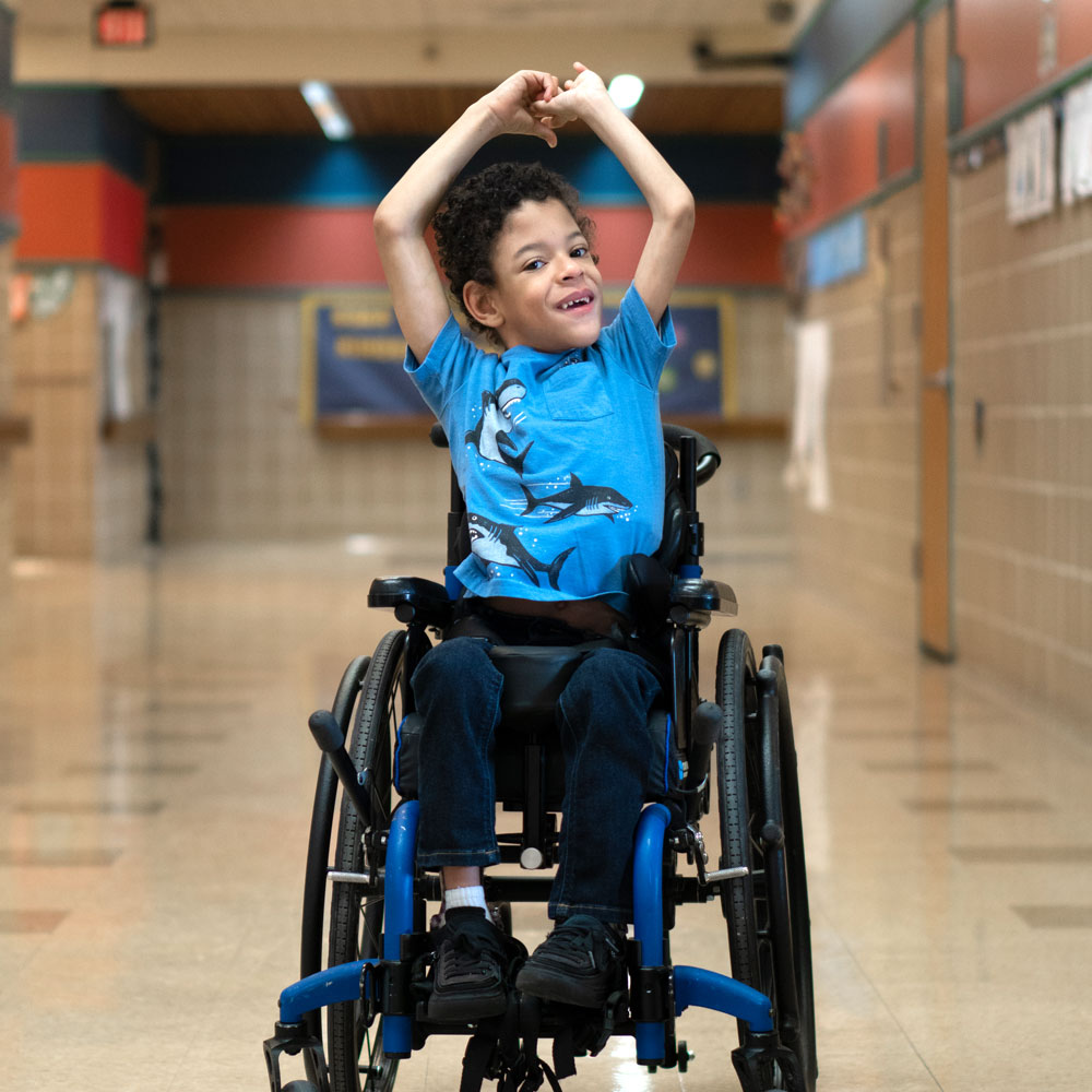 A boy in a wheelchair with smiling with his arms in the air.