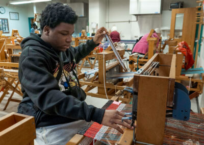 A young man weaves a project on a loom.