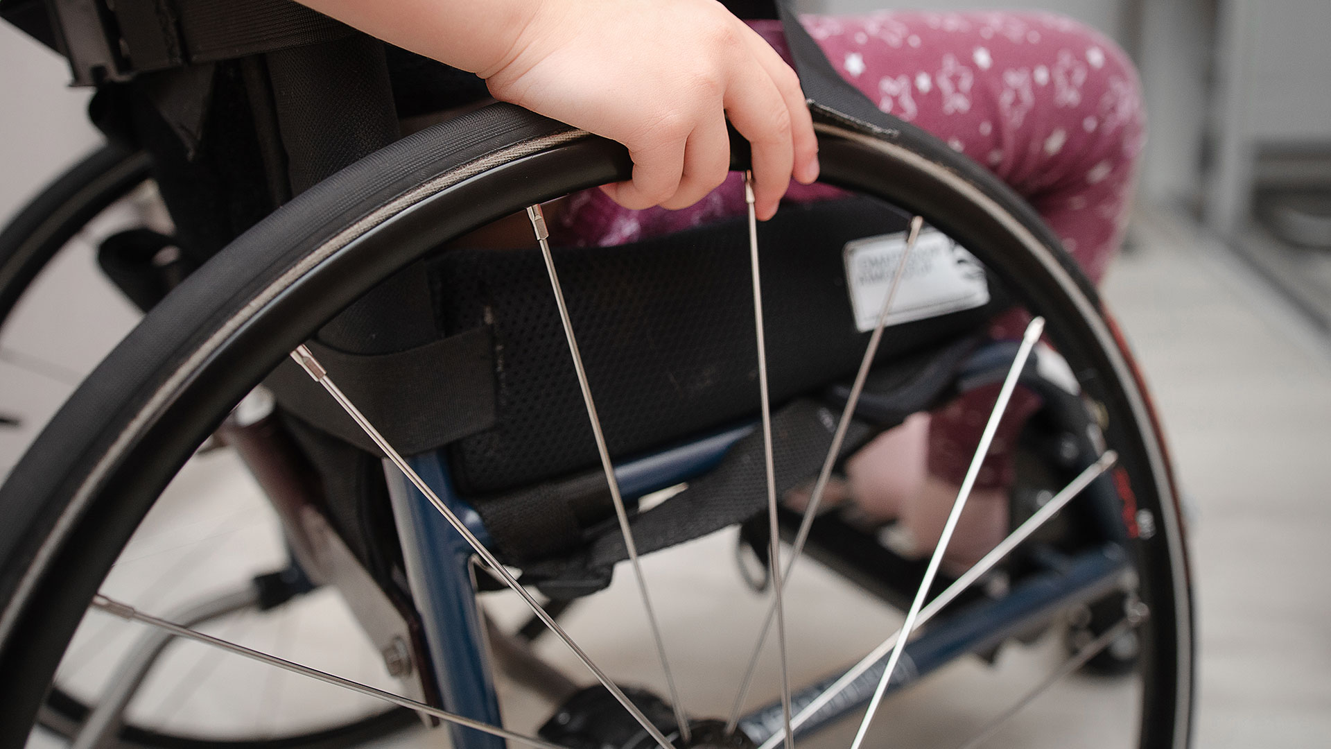Close up of a child's hand on the wheel of a wheelchair.