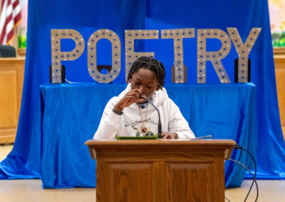 A student speaks at a podium with "Poetry" in large letters behind them.