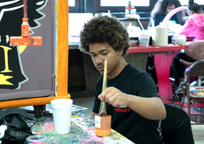 A boy in a classroom painting a cabinet.