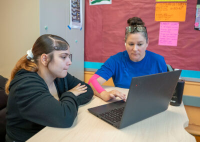 A teacher and student look at a computer.