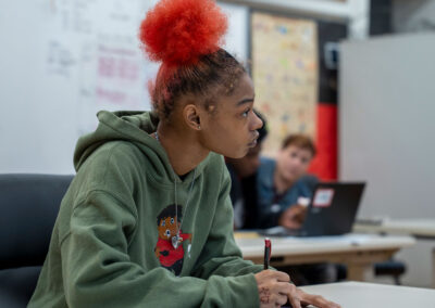 A girl with bright hair in a classroom, ready to write.
