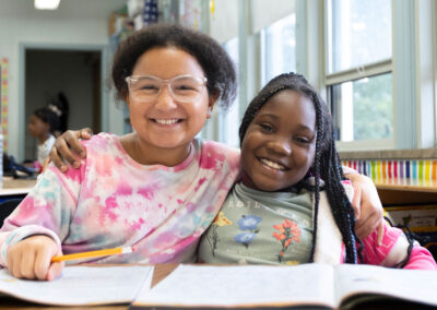 Two students at a table with their arms around one another.