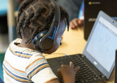 A young student with headphones uses a computer.