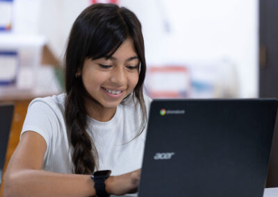 A girl smiles as she types on her laptop.